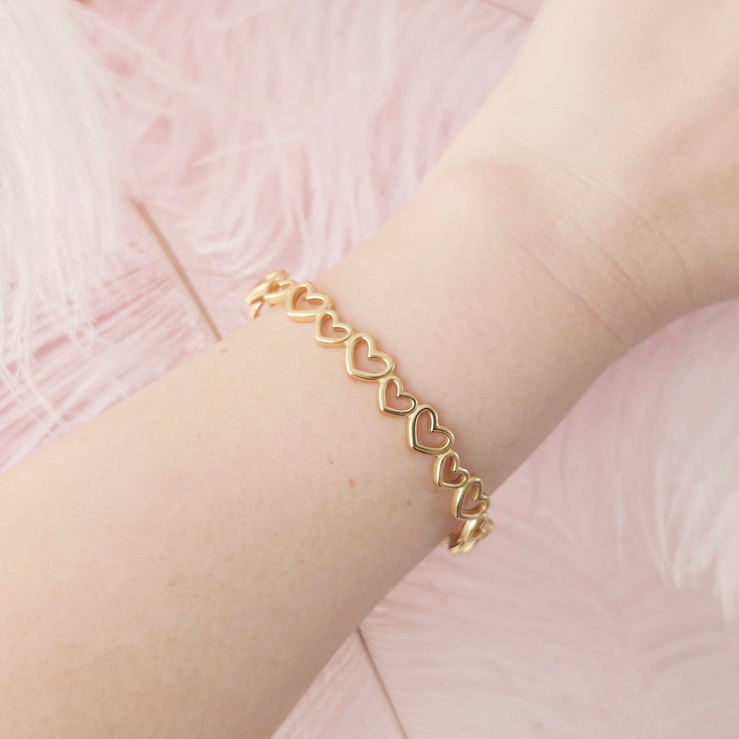 Gold bracelet with heart links on a wrist against a pink background