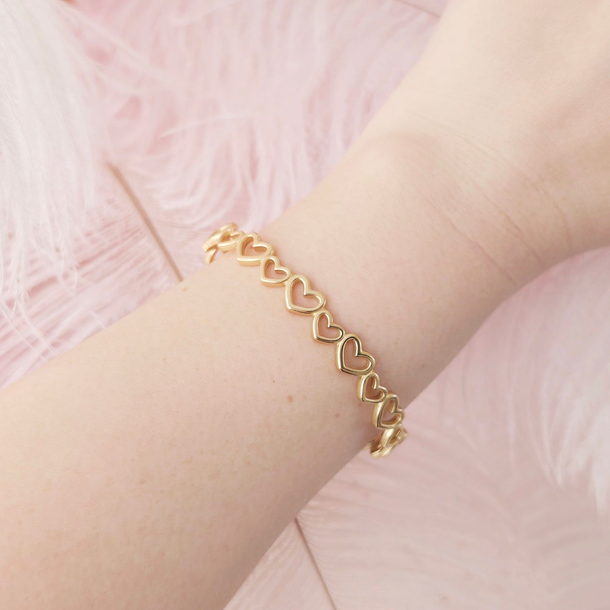Gold bracelet with heart links on a wrist against a pink background