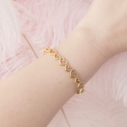 Gold bracelet with heart links on a wrist against a pink background