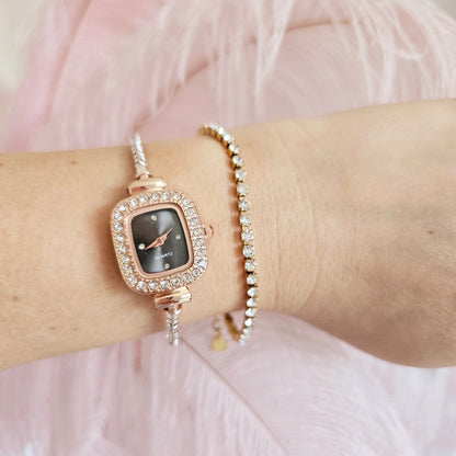Rose gold watch with black face on a wrist against a pink feathered background