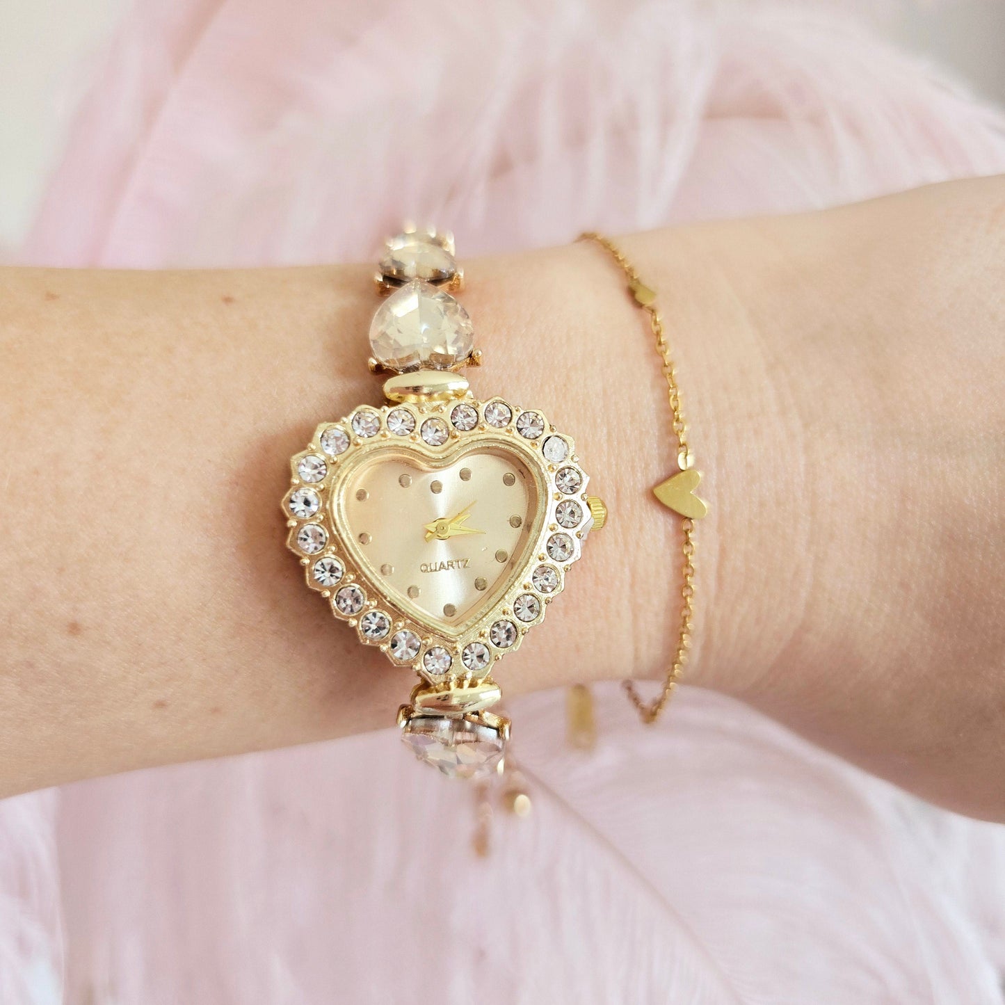 Gold heart-shaped watch on a wrist with a pink background